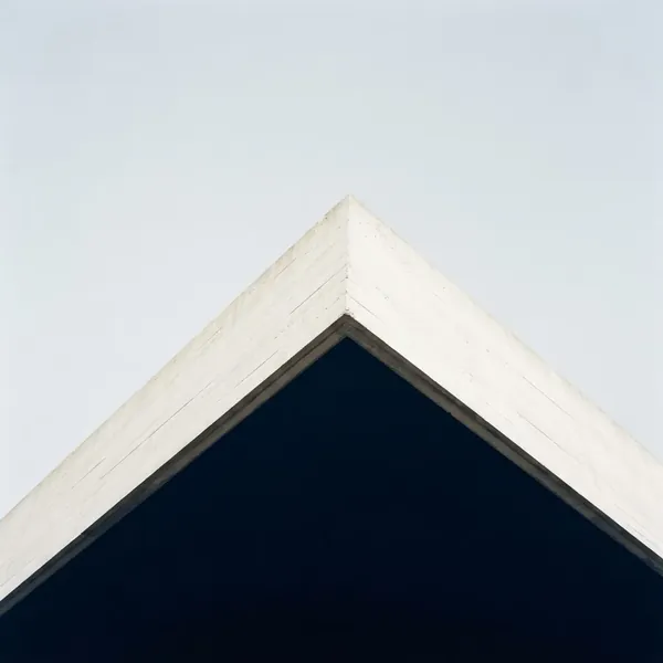Upward view of a clean angular building roofline against a pale blue sky